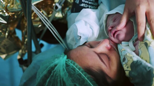Mother Holds Newborn Baby in Hospital. Mother Holding Her Newborn Baby on Her Chest Just After Delivery. First Sight of Mom and Her Newborn in Operation Room. Modern Hospital Operation Room
