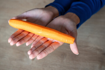 The woman holds food in her hand. the girl holds carrots in her hands. Orange carrot in hand
