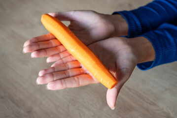 The woman holds food in her hand. the girl holds carrots in her hands. Orange carrot in hand