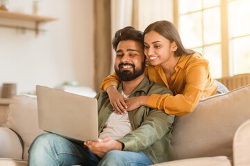 Young hindu couple using laptop, woman embracing man from behind