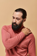 Obraz premium portrait, serious good looking man with beard posing in pink turtleneck jumper on beige background