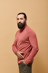 portrait, focused and handsome man with beard posing in pink turtleneck jumper on beige background