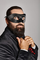 Obraz premium Christmas Masquerade, handsome bearded man in carnival mask and elegant suit on grey backdrop