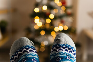 Close up of feet wearing warm Christmas socks with illuminated Christmas tree on the back ground