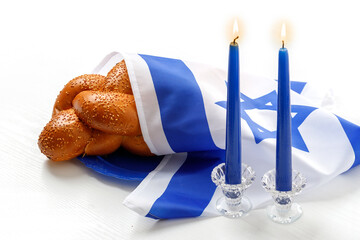 Challah bread covered with the Israeli flag, burning blue candles against a white background....