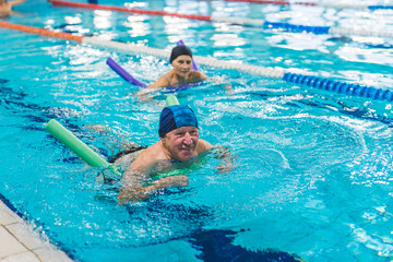 A mature couple playing with foam noodles in swimming pool. High quality photo