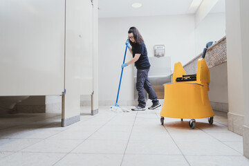 cleaning woman mopping a bathroom using a yellow bucket