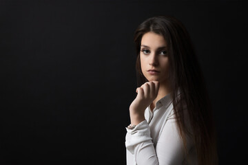 Portrait of beautiful  pensive long haired brunette girl  posing in studio on black background.  Horizontally. 