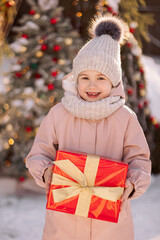 Little girl with a Christmas gift outdoors in winter on Christmas Eve. New Year background for holiday sale or promotion.