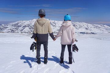 Back view of a couple holding hands while standing on snow in winter