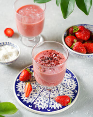 two glasses of strawberry smoothie, on a gray concrete background, next to a bowl of berries