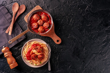 Meatballs. Beef meat balls, overhead flat lay shot in a pan and with a plate of spaghetti pasta, on a black background, with copy space - obrazy, fototapety, plakaty