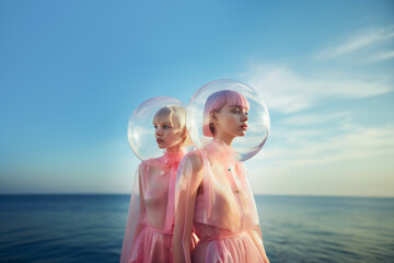 Portrait outdoor of two girls with transparent glass spheres ontheir heads wearing trendy modern clothes. Futuristic fashion style