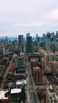 Aerial drone shot of downtown Toronto's skyline showcasing rising buildings, busy streets, and Lake Ontario in the distant background. Prominent landmarks and construction cranes in view. 