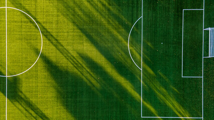 Soccer field with goal and penalty area from above. Overhead view of the penalty area of a football pitch with synthetic grass. No people. Sunset background texture - obrazy, fototapety, plakaty