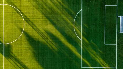 Tableaux sur verre Herbe Soccer field with goal and penalty area from above. Overhead view of the penalty area of a football pitch with synthetic grass. No people. Sunset background texture