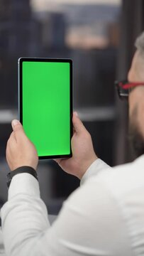 Bearded Man in Glasses Using Tablet Computer with Green Screen Mock Up Display. Male Watching Videos and Reading Social Media Posts on Mobile Device. Shooting Close Up Over the Shoulder