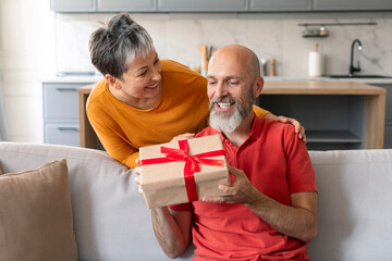Loving wife surprising her mature husband with gift at home