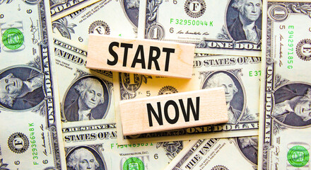 Start now symbol. Concept words Start now on beautiful wooden block. Beautiful background from dollar bills. Dollar bills. Business marketing, motivational start now concept. Copy space.