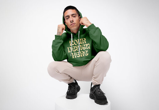 Mockup of young man wearing hoodie with customizable color, crouching