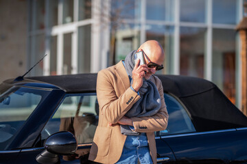 asual mature man using mobile phone and standing next to his car