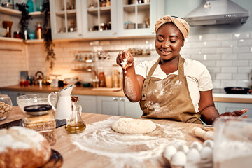 Art of baking. Black housewife in turban sprinkling dough with flour during baking process at...