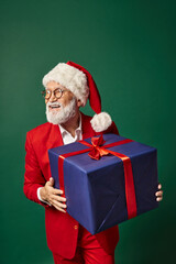 cheerful man dressed as Santa holding huge present smiling and looking away, Christmas concept