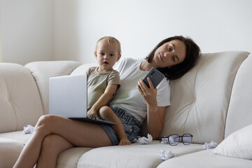 Obraz premium Young girl sitting on the couch and trying to work next to the child. Procrastination and deadline at work