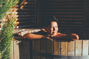 Young woman relaxing in wooden hot tub outdoor. SPA and health care concept. 