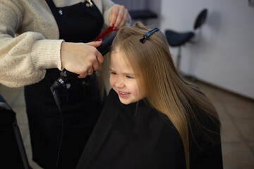 Fototapeta premium the hairdresser in the barbershop combing the hair of a little cute girl