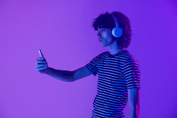 Latin man in headphones illuminated in purple viewing smartphone