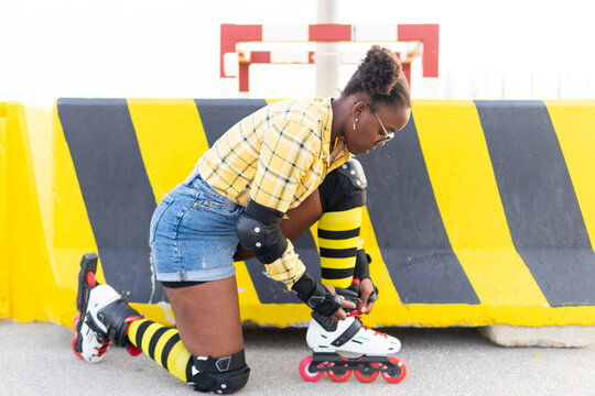 Young Woman Wearing Roller Skate Shoe While Kneeling At Skate Park