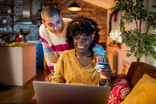 Lesbian couple enjoying a cozy evening together, shopping online in a festive living room