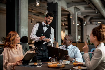 Attentive Waiter Assisting Guests with Menu Choices in Hotel Restaurant
