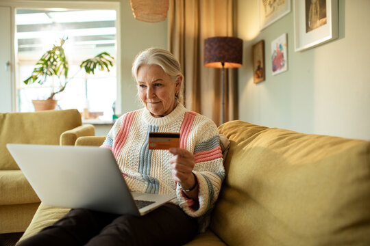 Elderly woman holding a credit card with laptop on the sofa at home