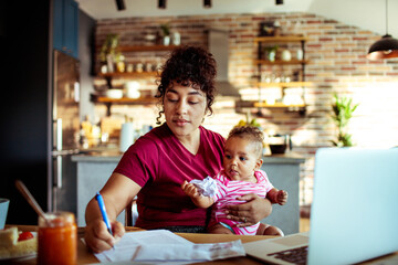 Focused mother multitasking between work and baby in a cozy kitchen