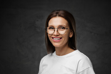 Delighted female in spectacles and white tee beams brightly with a moody backdrop