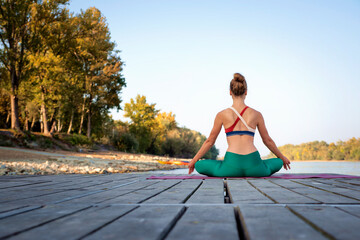 Rear view of a woman is meditating sitting in lotus position on yoga mat outdoor