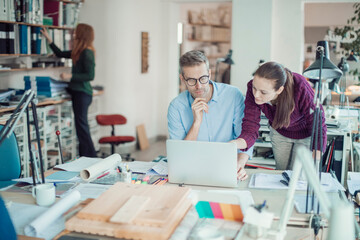 Obraz premium Two focused professionals discussing a project on a laptop in a modern workspace