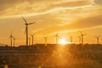 Windmill silhouettes at sunset. Power generation plant view from a car window. Renewable energy...