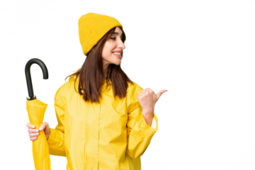Young caucasian woman with rainproof coat and umbrella over isolated chroma key background pointing to the side to present a product