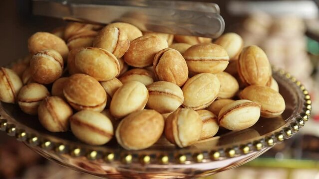 Close up pile of baked sweet cookies at nuts shape filled boiled condensed milk, caramel or cream on golden plate on candy bar at restaurant. Eastern Europe traditional homemade crunchy pastry.