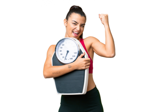 Young beauty woman over isolated chroma key background with weighing machine and doing victory gesture - Powered by Adobe