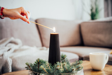Female hand lighting a candle with a match in winter cozy composition for hygge home mood. Black...