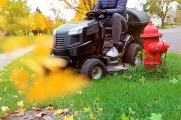 Mowing the grass with a lawn  tractor mower in sunny autumn. Gardener cuts the lawn in the garden