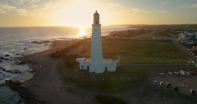 Aerial shot from a drone, open plan, of the Lighthouse located in Uruguay on a clear day. This lighthouse is located in the town of La Paloma. The sun is setting behind. It's a short shot of the light