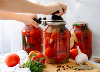 female hands screw the lid onto a jar of tomatoes with a special machine on the kitchen table
