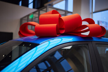 The new car is wrapped in a red bow. Beautiful gift concept. - obrazy, fototapety, plakaty