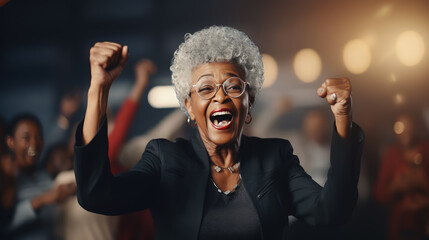 Excited elderly businesswoman celebrating success in office. Cheerful mature woman looking at camera with open mouth and hands raised. Happy african american female senior rejoices achievement - Powered by Adobe