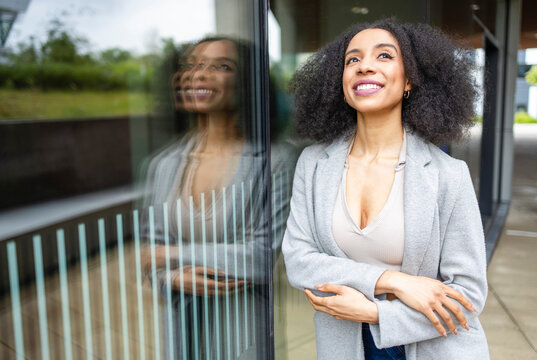 Ethnic young woman smiling and leaning against a reflective glass pane